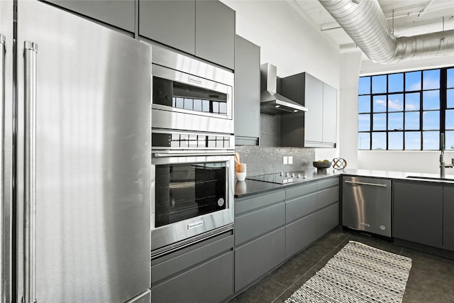 kitchen with gray cabinetry, wall chimney range hood, stainless steel appliances, and sink