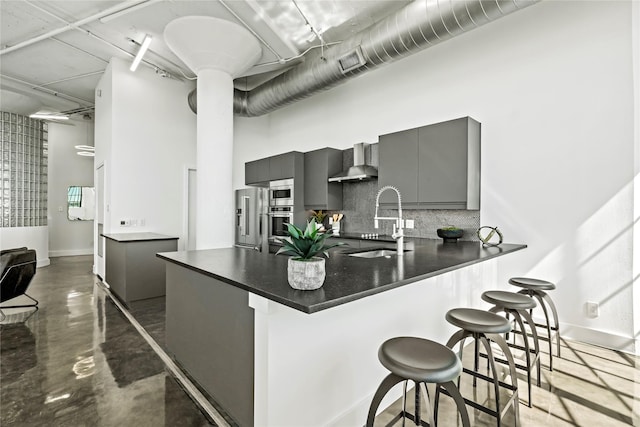 kitchen featuring sink, gray cabinetry, a kitchen bar, kitchen peninsula, and wall chimney exhaust hood