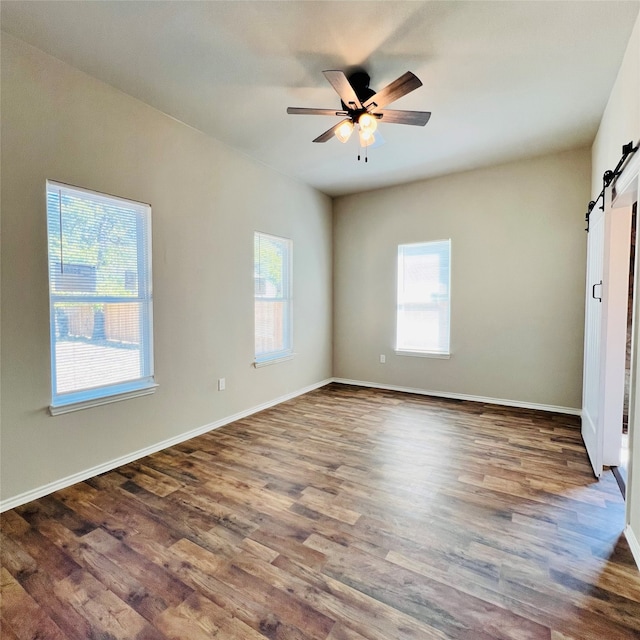 unfurnished room with dark hardwood / wood-style floors, a barn door, and ceiling fan