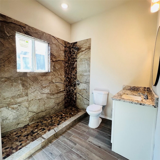 bathroom with toilet, hardwood / wood-style floors, vanity, and a tile shower