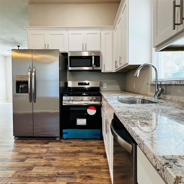 kitchen with stainless steel appliances, sink, light stone countertops, white cabinetry, and dark hardwood / wood-style flooring