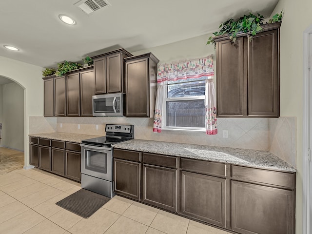 kitchen featuring appliances with stainless steel finishes, light stone counters, dark brown cabinets, and light tile patterned floors