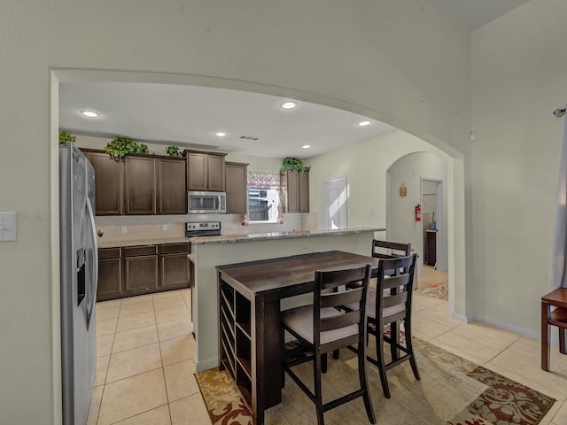 kitchen with appliances with stainless steel finishes, light tile patterned flooring, light stone countertops, and a center island