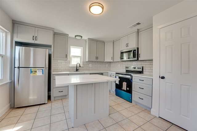 kitchen featuring backsplash, appliances with stainless steel finishes, light tile patterned flooring, sink, and a center island