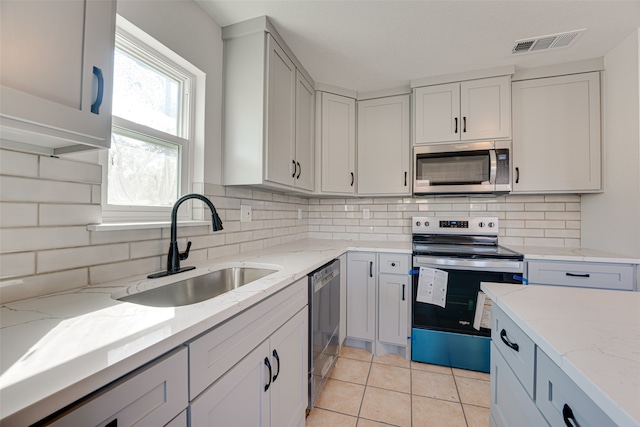 kitchen featuring appliances with stainless steel finishes, sink, light tile patterned flooring, light stone counters, and decorative backsplash