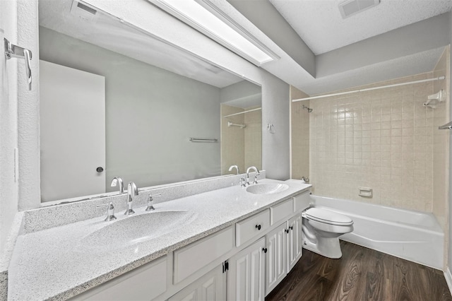 full bathroom featuring a textured ceiling, wood-type flooring, toilet, vanity, and tiled shower / bath combo