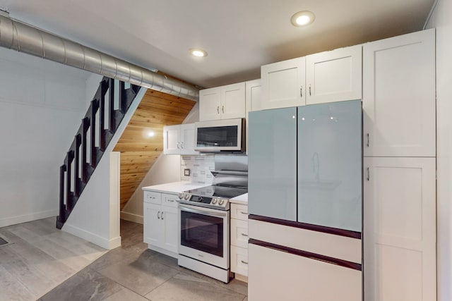 kitchen with white cabinetry, decorative backsplash, wooden walls, and white appliances