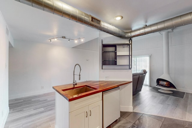 kitchen with wooden counters, white dishwasher, a wood stove, sink, and light wood-type flooring