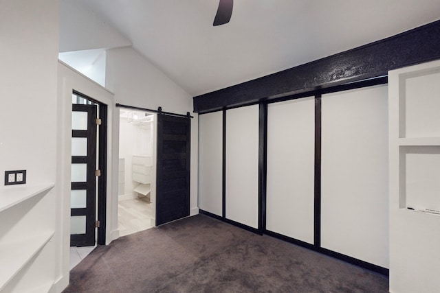 interior space featuring carpet flooring, ensuite bath, vaulted ceiling, a barn door, and ceiling fan