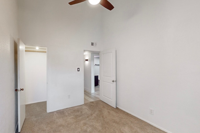 unfurnished bedroom featuring a towering ceiling, light colored carpet, and ceiling fan