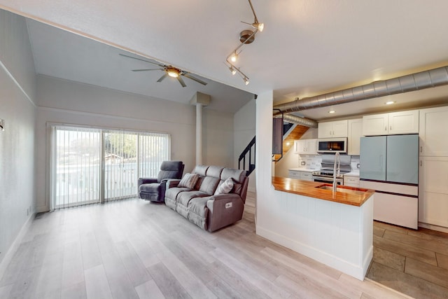 kitchen featuring stainless steel appliances, white cabinetry, light hardwood / wood-style floors, kitchen peninsula, and ceiling fan