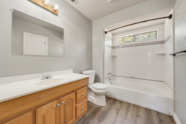 full bathroom featuring a textured ceiling, wood-type flooring, toilet, vanity, and tiled shower / bath combo