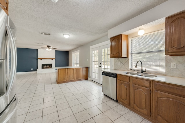 kitchen featuring sink, backsplash, a brick fireplace, stainless steel appliances, and light tile patterned floors