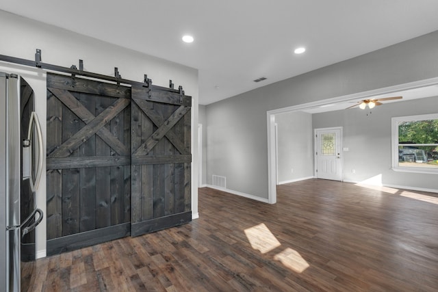 empty room with dark wood-type flooring, ceiling fan, and a barn door