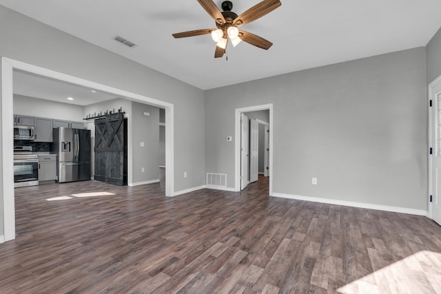 unfurnished living room with dark wood-type flooring, ceiling fan, and a barn door