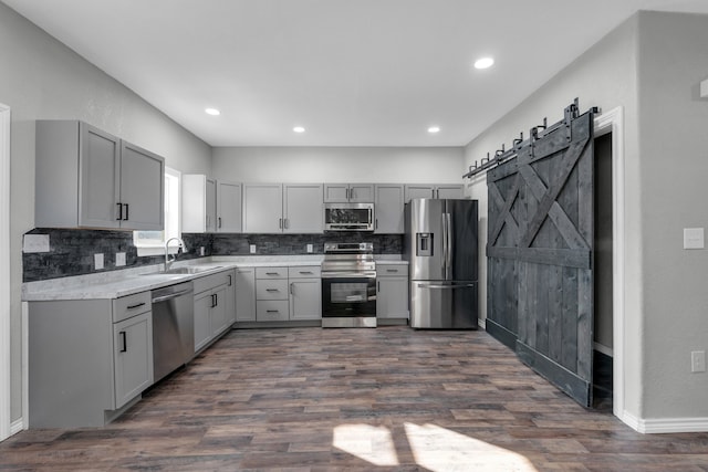 kitchen with gray cabinetry, stainless steel appliances, sink, a barn door, and dark hardwood / wood-style flooring