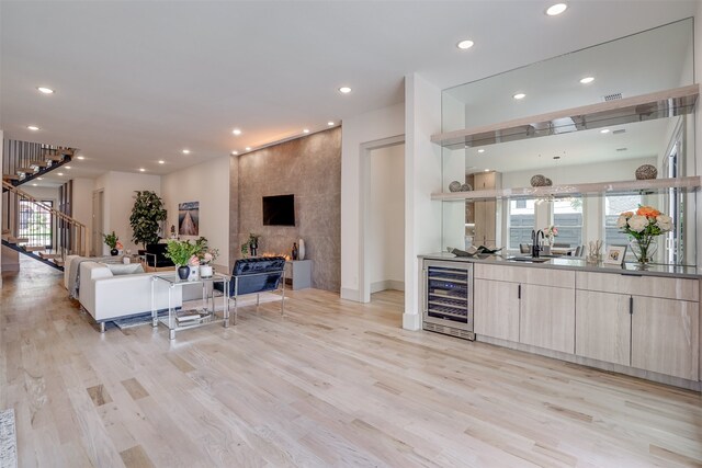 bar featuring wine cooler, sink, a fireplace, and light wood-type flooring