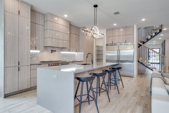 kitchen featuring appliances with stainless steel finishes, sink, light hardwood / wood-style floors, and a large island with sink