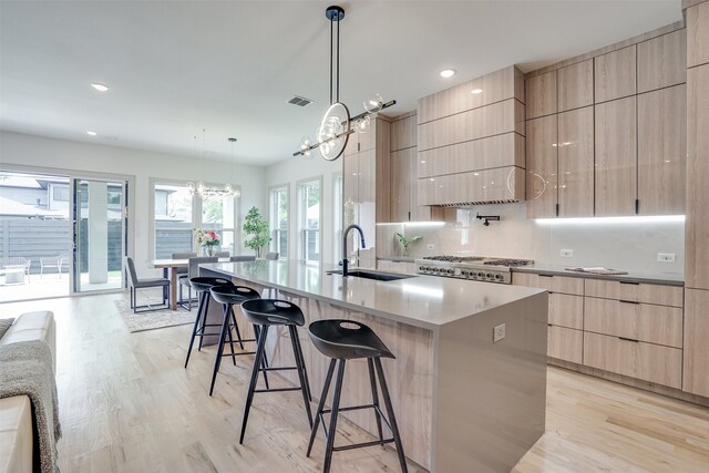 kitchen featuring sink, an island with sink, hanging light fixtures, and light hardwood / wood-style floors