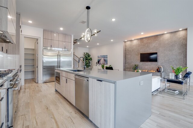 kitchen with wall chimney range hood, a large island, sink, decorative light fixtures, and appliances with stainless steel finishes