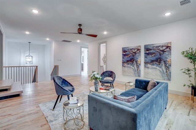 living room with ceiling fan with notable chandelier and light hardwood / wood-style floors