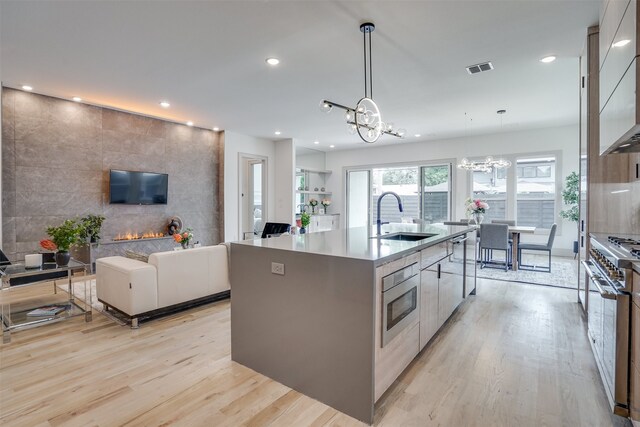 kitchen with an inviting chandelier, a kitchen island with sink, light hardwood / wood-style flooring, sink, and decorative light fixtures