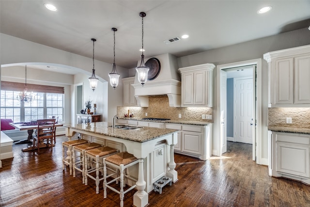 kitchen with dark wood-type flooring, light stone counters, and a kitchen island with sink