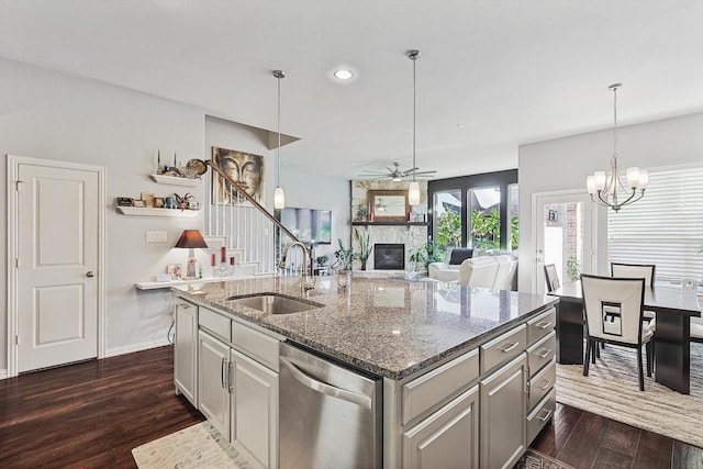 kitchen featuring sink, dishwasher, an island with sink, dark hardwood / wood-style flooring, and a stone fireplace