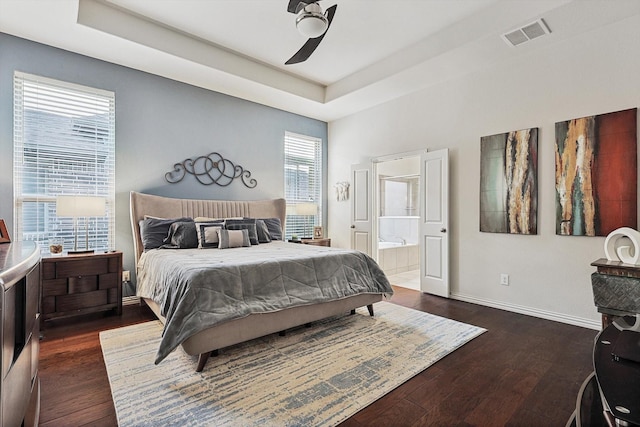 bedroom with connected bathroom, dark hardwood / wood-style flooring, ceiling fan, and a tray ceiling