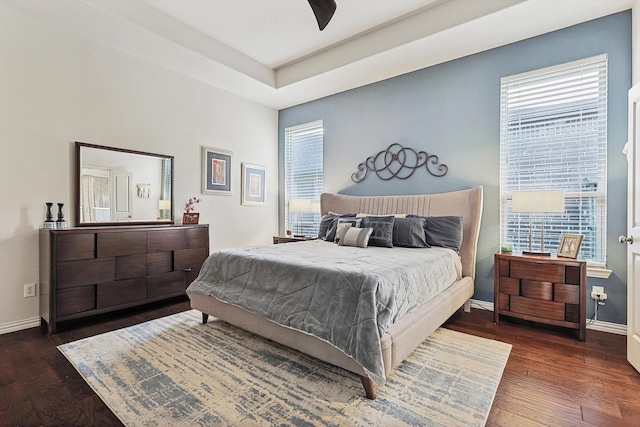 bedroom with ceiling fan, multiple windows, dark hardwood / wood-style floors, and a tray ceiling