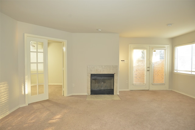 unfurnished living room featuring french doors, a tile fireplace, and light colored carpet