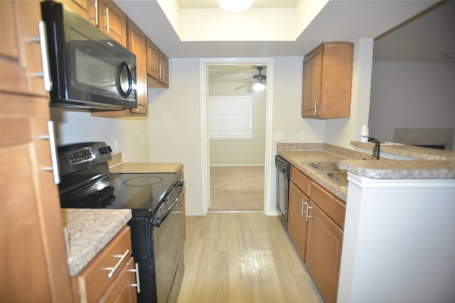 kitchen featuring black appliances, sink, light wood-type flooring, a raised ceiling, and ceiling fan