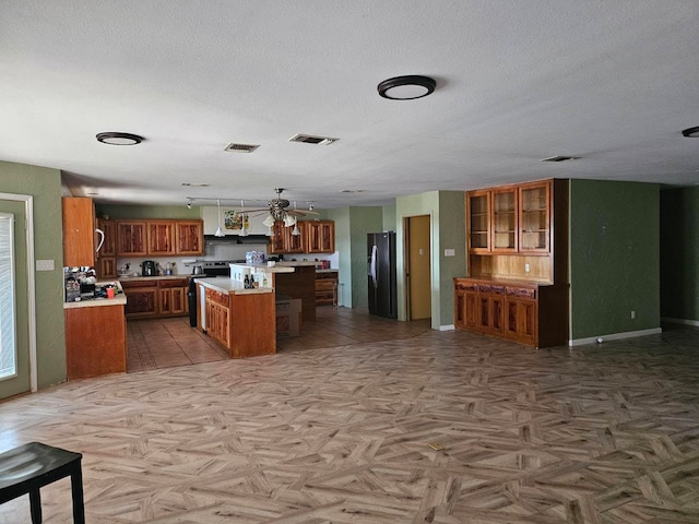 kitchen with a textured ceiling, a center island, hanging light fixtures, and black refrigerator with ice dispenser