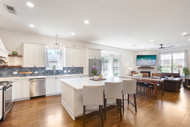 kitchen with stainless steel appliances, decorative light fixtures, white cabinets, hardwood / wood-style floors, and a center island