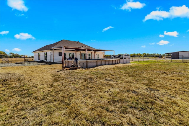 back of property with a rural view and a yard