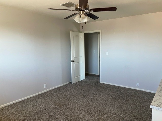 unfurnished room with ceiling fan and dark colored carpet