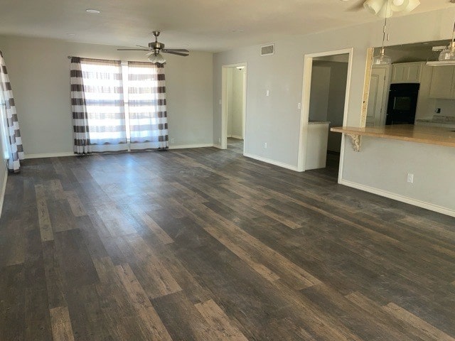 unfurnished living room featuring dark wood-type flooring and ceiling fan