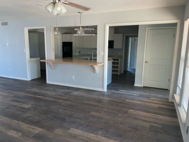 kitchen featuring kitchen peninsula, decorative light fixtures, a breakfast bar area, dark hardwood / wood-style floors, and black refrigerator