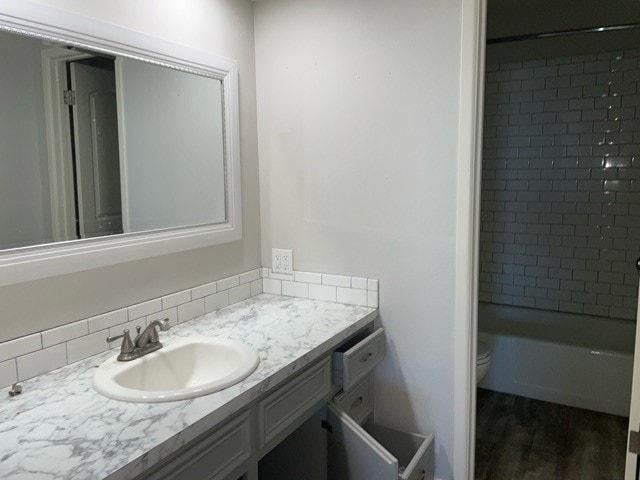 full bathroom featuring decorative backsplash, hardwood / wood-style flooring, toilet, tiled shower / bath, and vanity