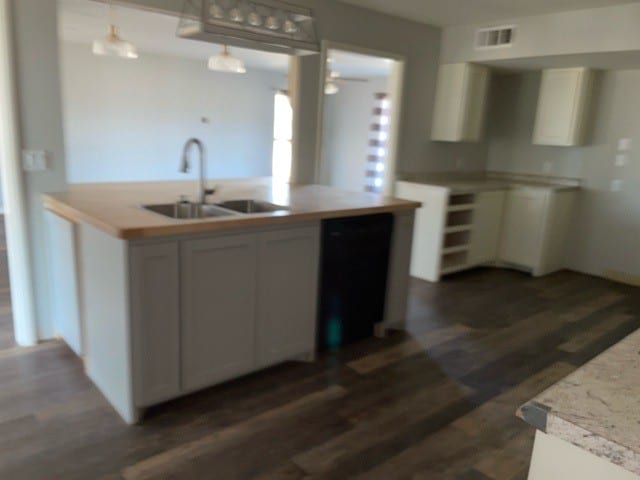 kitchen featuring black dishwasher, dark wood-type flooring, sink, decorative light fixtures, and white cabinetry