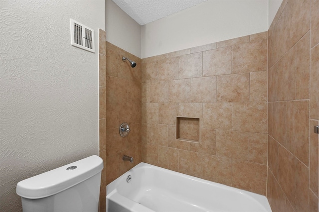 bathroom featuring toilet, tiled shower / bath combo, and a textured ceiling