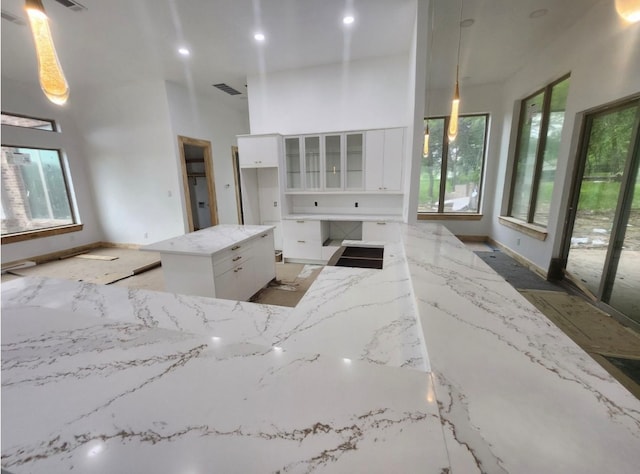 kitchen with white cabinetry, light stone counters, decorative light fixtures, and plenty of natural light