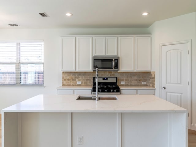 kitchen with white cabinets, light stone countertops, stainless steel appliances, and a center island with sink