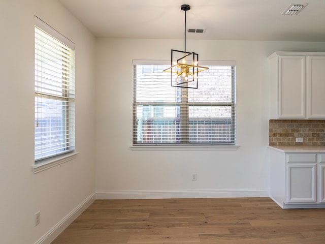 unfurnished dining area with light hardwood / wood-style flooring, a chandelier, and plenty of natural light