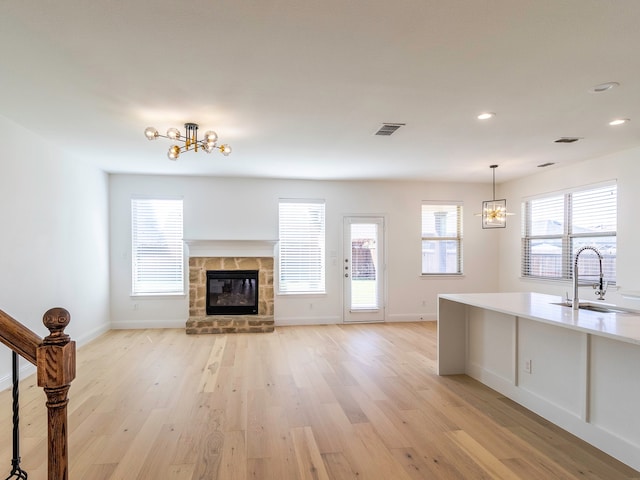 unfurnished living room featuring sink, a stone fireplace, light wood-type flooring, and a healthy amount of sunlight