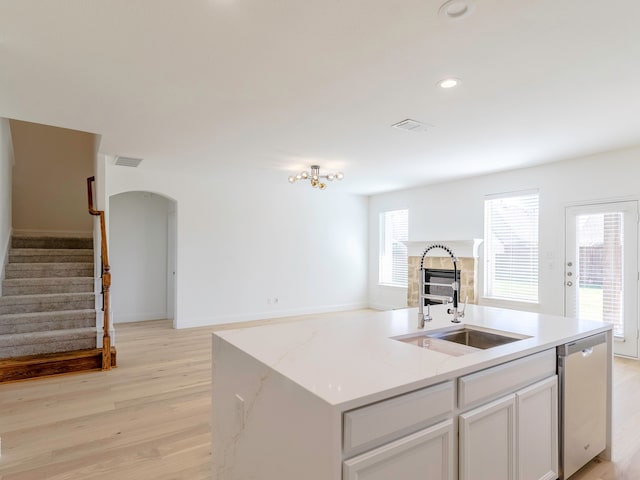 kitchen with stainless steel dishwasher, sink, an island with sink, and light hardwood / wood-style floors