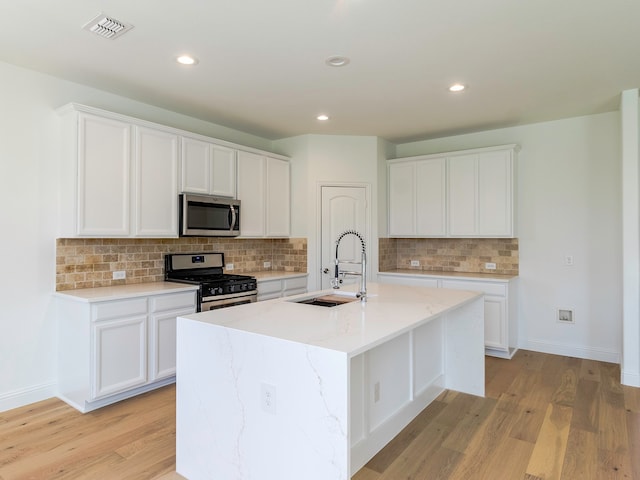 kitchen with appliances with stainless steel finishes, a kitchen island with sink, sink, and light wood-type flooring