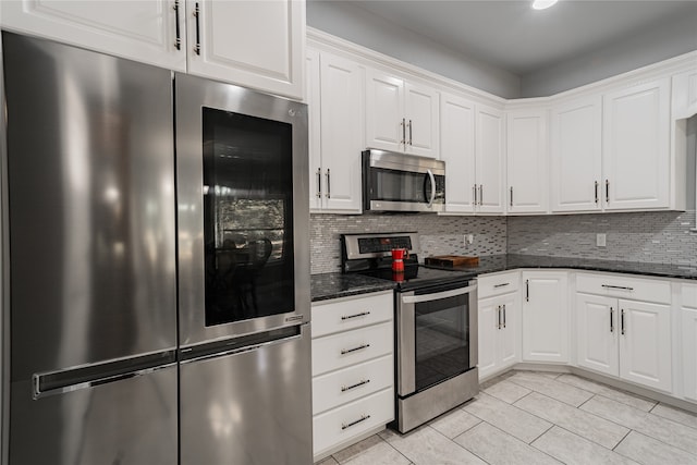 kitchen with white cabinetry, stainless steel appliances, backsplash, and dark stone counters