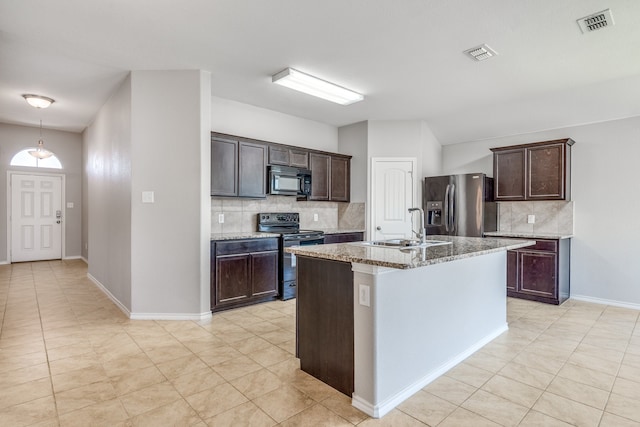 kitchen featuring black range with electric stovetop, stainless steel fridge, an island with sink, and tasteful backsplash