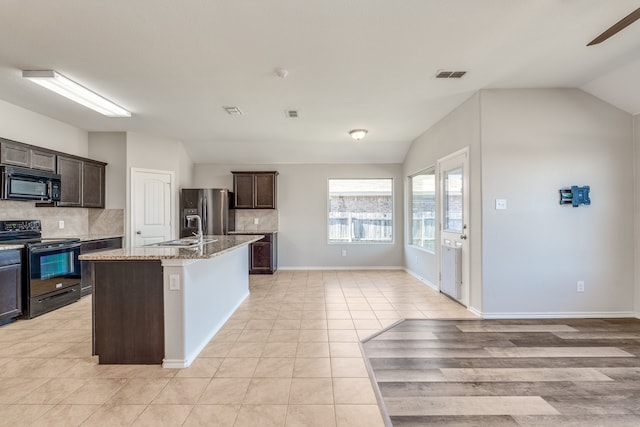 kitchen with light stone counters, black appliances, lofted ceiling, and an island with sink